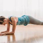 Full body sportive female in activewear doing Forearm plank on floor while training yoga asana in light room at home